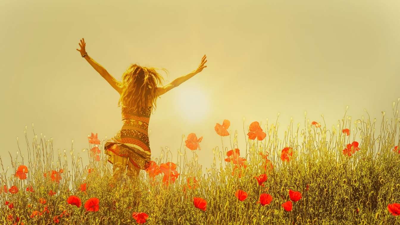 Woman running through poppy field with arms in freedom pose